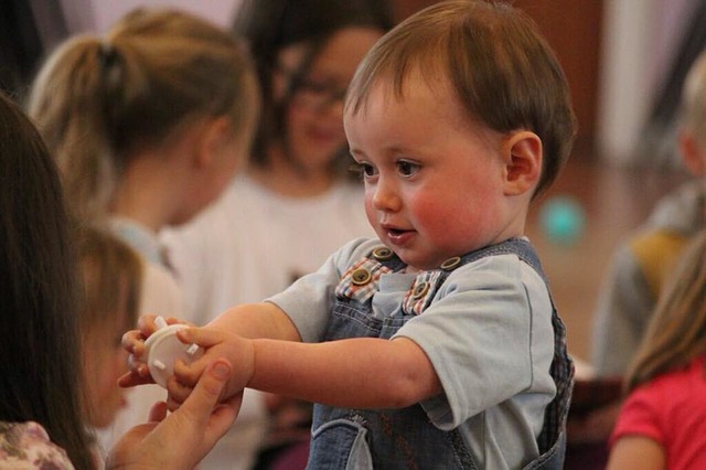 A young boy hands another child a toy while looking at her.