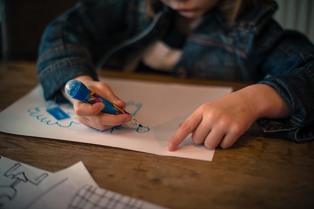 Child drawing on a piece of paper with a marker at a desk.