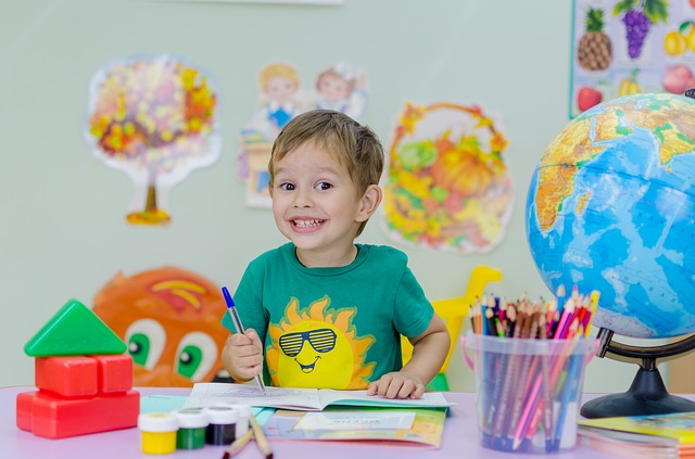 Happy child drawing in a book and sitting at a desk with a globe to his left.